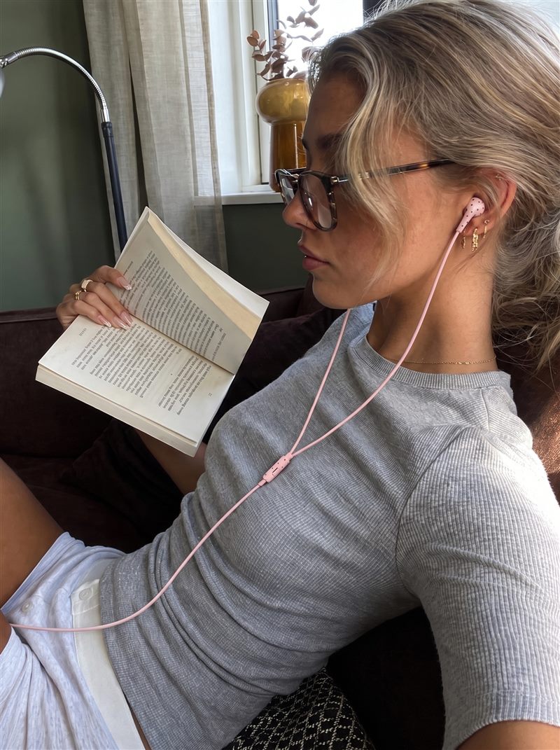 Vrouw met bril leest een boek op de bank met roze oortjes