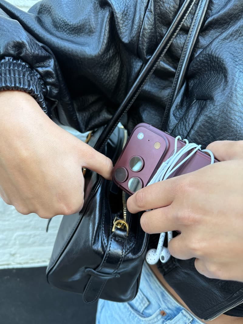Telefoon met opgerolde witte oortjes met stipjes gaat in een zwarte leren tas