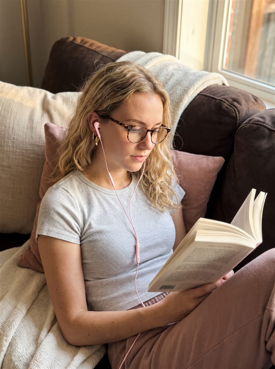 Vrouw met bril leest een boek op de bank met roze oortjes