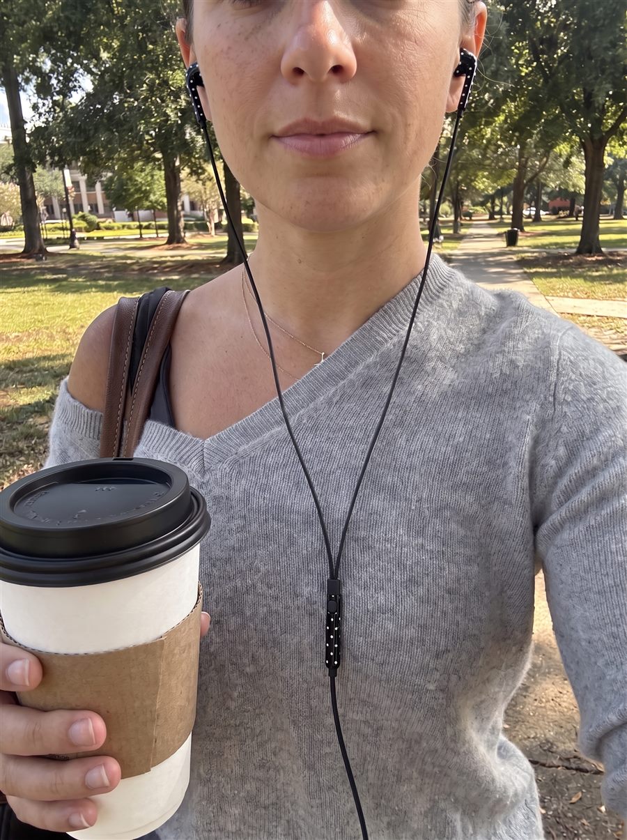 Selfie in grijze trui met koffie in het park en zwarte oortjes met witte stipjes